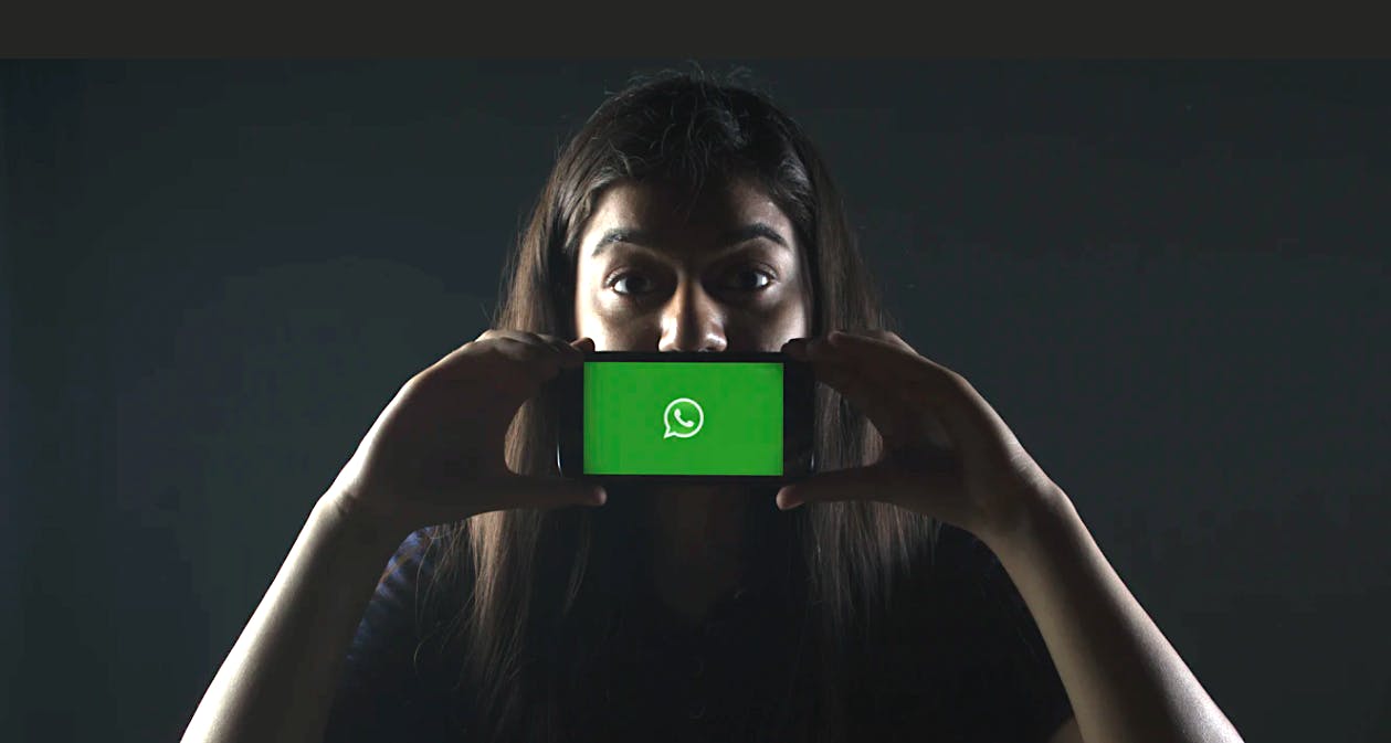 woman holding up smartphone displaying the green WhatsApp messenger logo